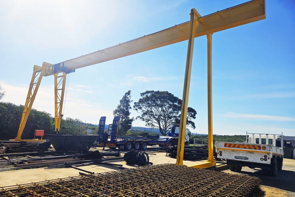 Yellow gantry crane over the steel yard at RMS East London, with welded mesh sheets and a low-bed trailer in view