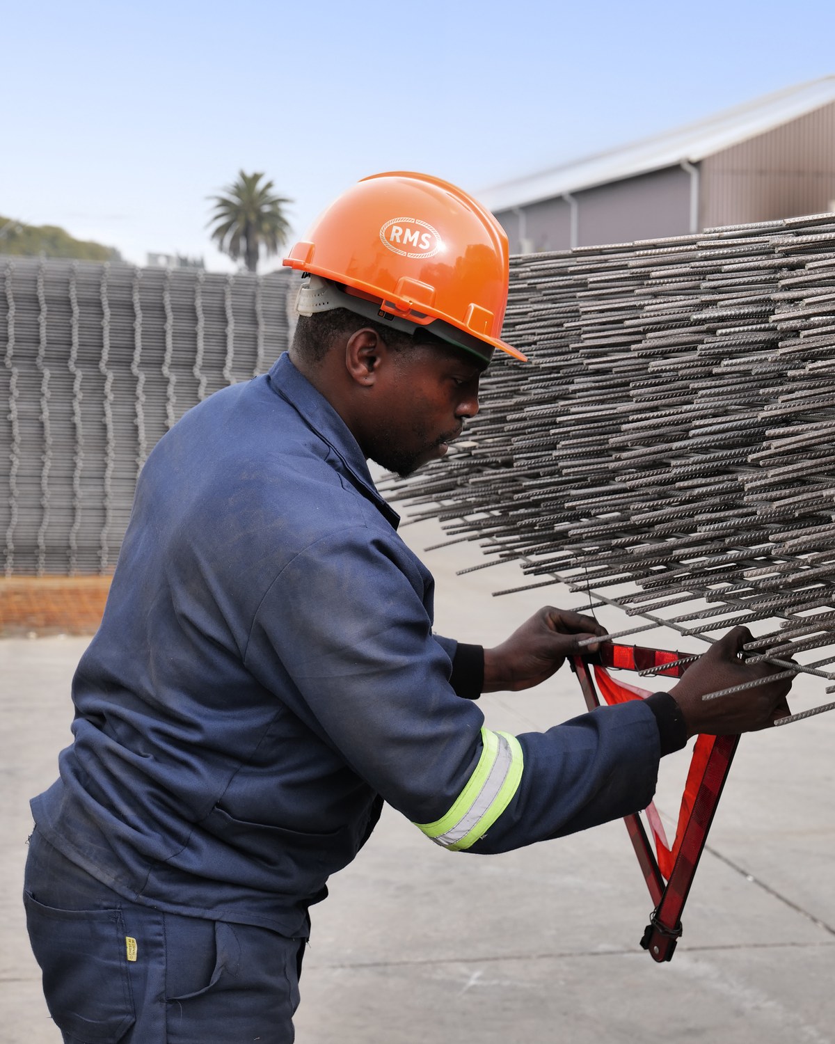 RMS team member in an orange RMS hard hat securing a warning triangle to the end of a welded mesh load